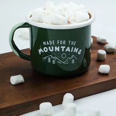 a green mug filled with marshmallows on top of a wooden board