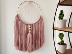 a pink macrame hanging on the wall next to potted plants and succulents