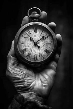 a person holding an old pocket watch in their hand, black and white photo with focus on the clock