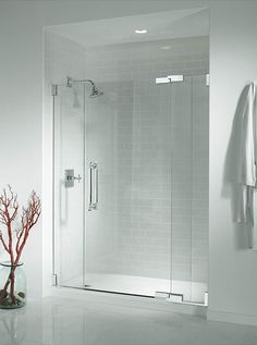 a white bathroom with a glass shower door and a vase with a red tree in it