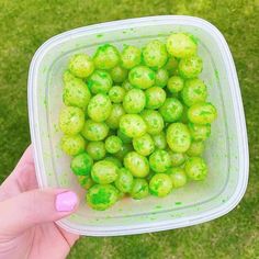 a person holding up a plastic container filled with green sprinkles on the grass