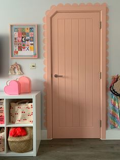 a pink door in the corner of a room next to a white shelf with bags on it