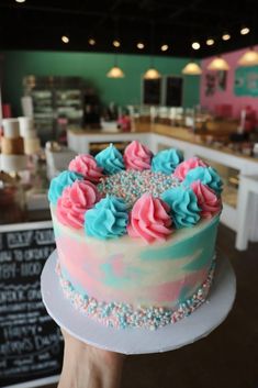 a person holding up a cake with frosting and sprinkles on it