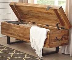 an open wooden trunk sitting on top of a floor next to a rug and window