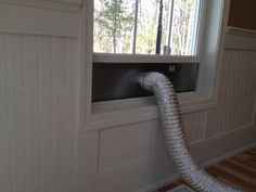 a silver hose sticking out of the side of a window next to a wooden floor