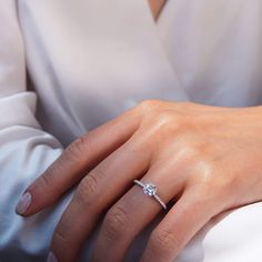 a woman's hand with a diamond ring on her left hand, wearing a white dress