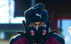 a man wearing a black hat and gloves with his hands covering his face in front of him