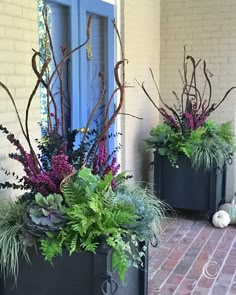 two black planters with purple flowers and greenery in them on the side of a building