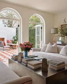 a living room filled with lots of furniture next to two large arched windows on top of a tiled floor