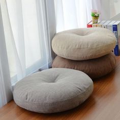 two round pillows sitting on top of a wooden table next to a bookcase and window