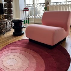 a pink chair sitting on top of a wooden floor next to a red and black rug