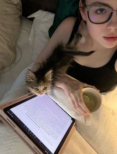 a woman with glasses holding a cat on her lap while looking at an electronic device