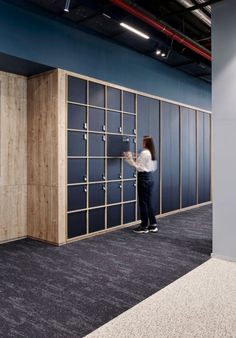 a woman standing in front of a blue wall with lots of wooden doors on it