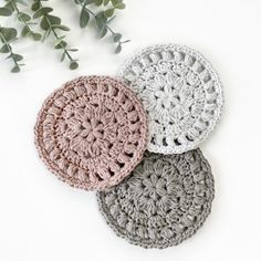 three crocheted coasters sitting on top of a table next to a plant