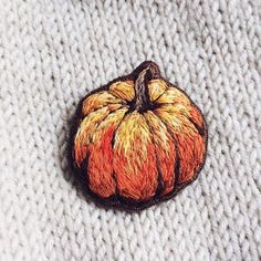 a small orange and yellow pumpkin sitting on top of a white knitted cloth covered surface