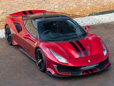 a red sports car with black stripes parked in front of a brick wall and door