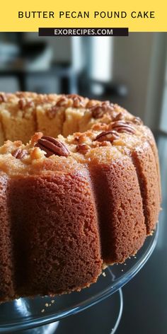 a bundt cake with pecans on top sitting on a glass platter next to a stove