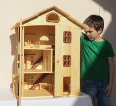 a young boy standing next to a wooden doll house