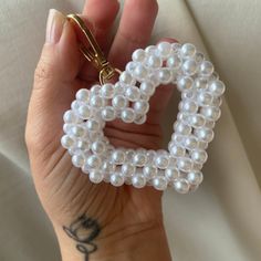 a hand holding a white beaded heart shaped keychain