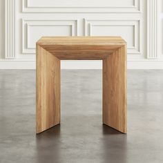 a small wooden table sitting on top of a cement floor next to a white wall