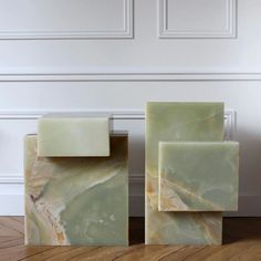 two green marble blocks sitting on top of a wooden floor in front of a white wall