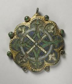 an ornate gold brooch with green and blue stones on it's back side