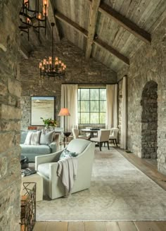 a living room filled with furniture and a chandelier hanging from the ceiling next to a stone wall