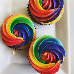 three cupcakes with rainbow frosting on a white plate