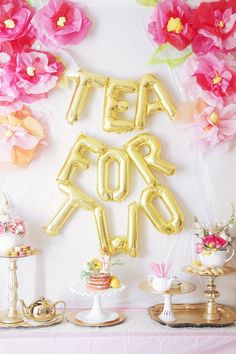 a table topped with balloons and flowers next to a sign that says tea for four