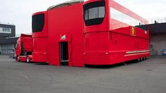 a large red bus sitting in a parking lot next to a tall white building with windows