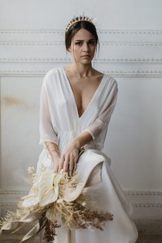 a woman in a white dress sitting on a chair with her hand on the bouquet