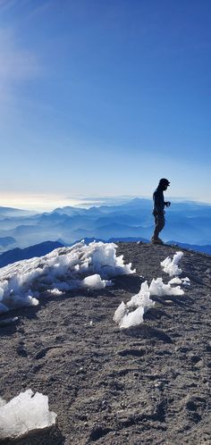 a person standing on top of a snow covered mountain with mountains in the back ground