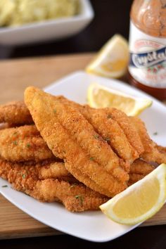 fried fish sticks on a white plate with lemon wedges next to dip and cole slaw