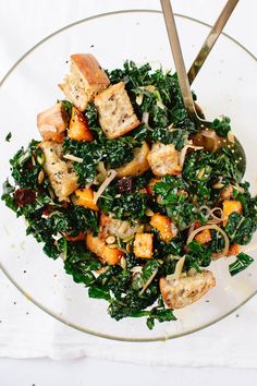 a glass bowl filled with greens and tofu on top of a white table cloth