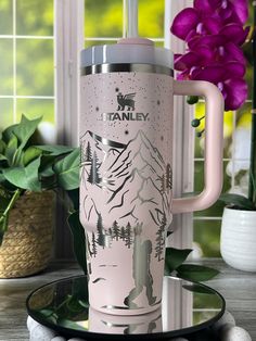 a pink travel mug sitting on top of a table next to a potted plant