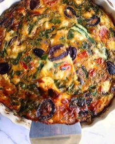 a casserole dish with cheese, olives and spinach in it next to a knife