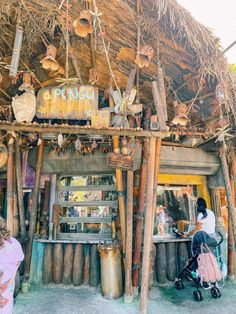 a woman sitting at a table in front of a hut with lots of items on it