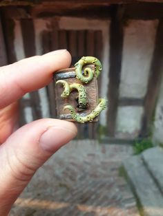 a person holding up a tiny ring with two green snakes on it's side