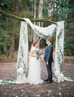 a bride and groom standing under an outdoor wedding ceremony arch with greenery on it