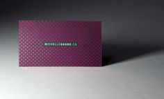 a pink business card sitting on top of a white table next to a gray wall