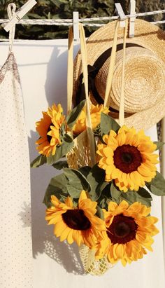 sunflowers in a vase on a clothesline with a straw hat hanging from it