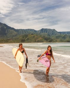 two women walking on the beach with surfboards