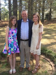 three people standing next to each other in front of trees