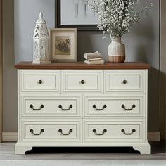 a white dresser with flowers and pictures on top