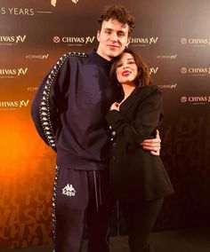 a man and woman standing next to each other in front of a red carpeted wall