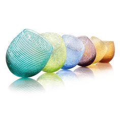 four different colored glass bowls lined up in a row on a white surface with reflections