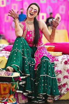 a woman sitting on top of a bed wearing a green and pink lehenga