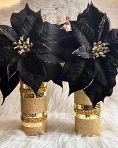 two black and gold vases with flowers in them on a white furnishing