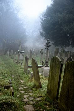 an old cemetery in the fog with tombstones and crosses on it's sides