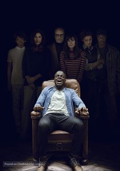 a man is sitting in a chair with his hands out and people standing behind him